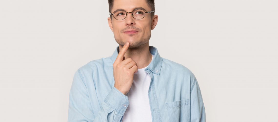 Thoughtful Caucasian young male in glasses touch chin with finger thinking or considering, pensive European man wearing spectacles isolated on grey studio background making decision or imagining