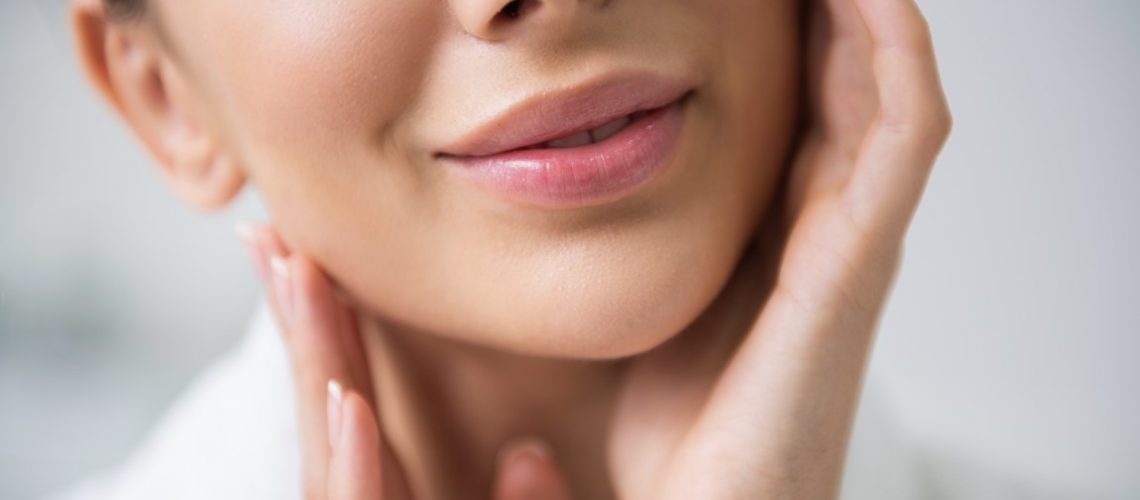 Health treatment. Close up face down portrait of young careful smiling brunette woman enjoying her soft skin while tenderly touching face
